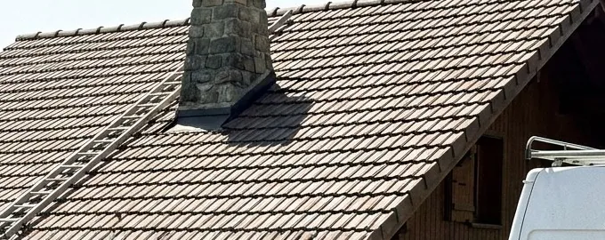 Toiture en tuiles brunes avec souche de cheminée en pierre, chantier des Toits du Chablais à Draillant